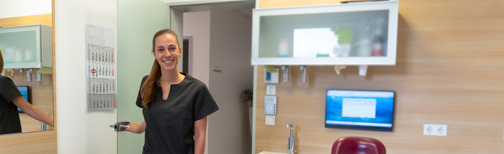 Assistenzzahnärztin öffnet die Glastür und begrüßt eine Patientin im modernen Behandlungszimmer.